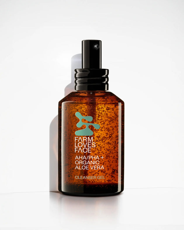 Bernsteinfarbene Flasche mit schwarzer Pumpe, beschriftet mit „Farm Loves Face AHA/PHA + Bio-Aloe Vera Reinigungsgel“, aufrecht auf einer weißen Oberfläche, dahinter leichter Schatten.