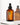 Eine braune Pumpflasche Farm Loves Face AHA/PHA + Bio-Aloe Vera Reinigungsgel steht auf einer weißen Oberfläche mit einem weichen Schatten und einer Spiegelung im Hintergrund.
